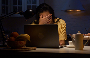 Woman holding her hand over her face while sitting in front of a laptop feeling stress.